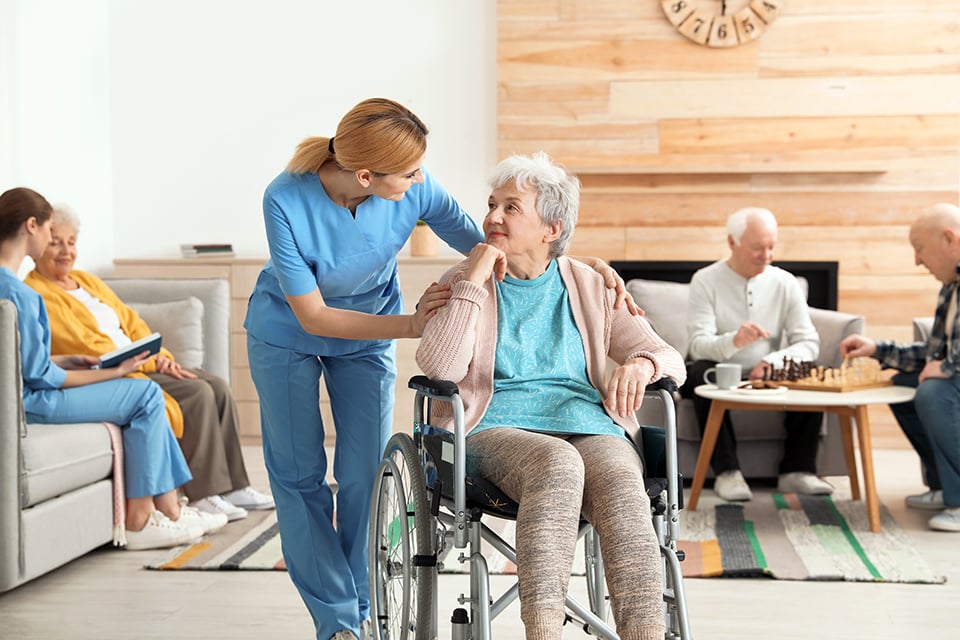 Woman nurse bending down to talk to an elderly patient in a wheelchair.