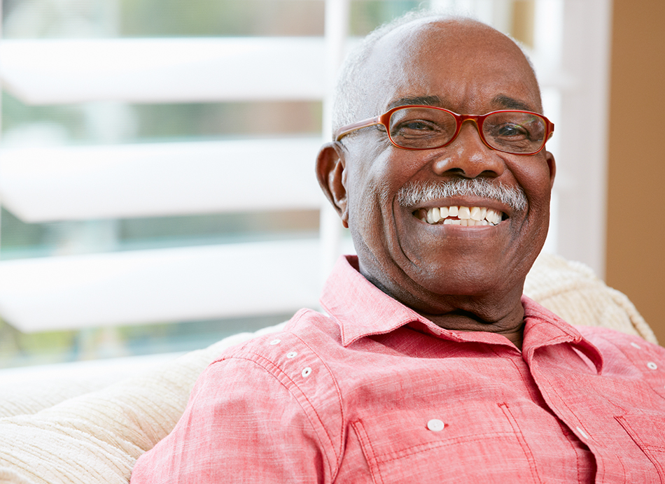 Senior man with a red shirt and red glasses, smiling.
